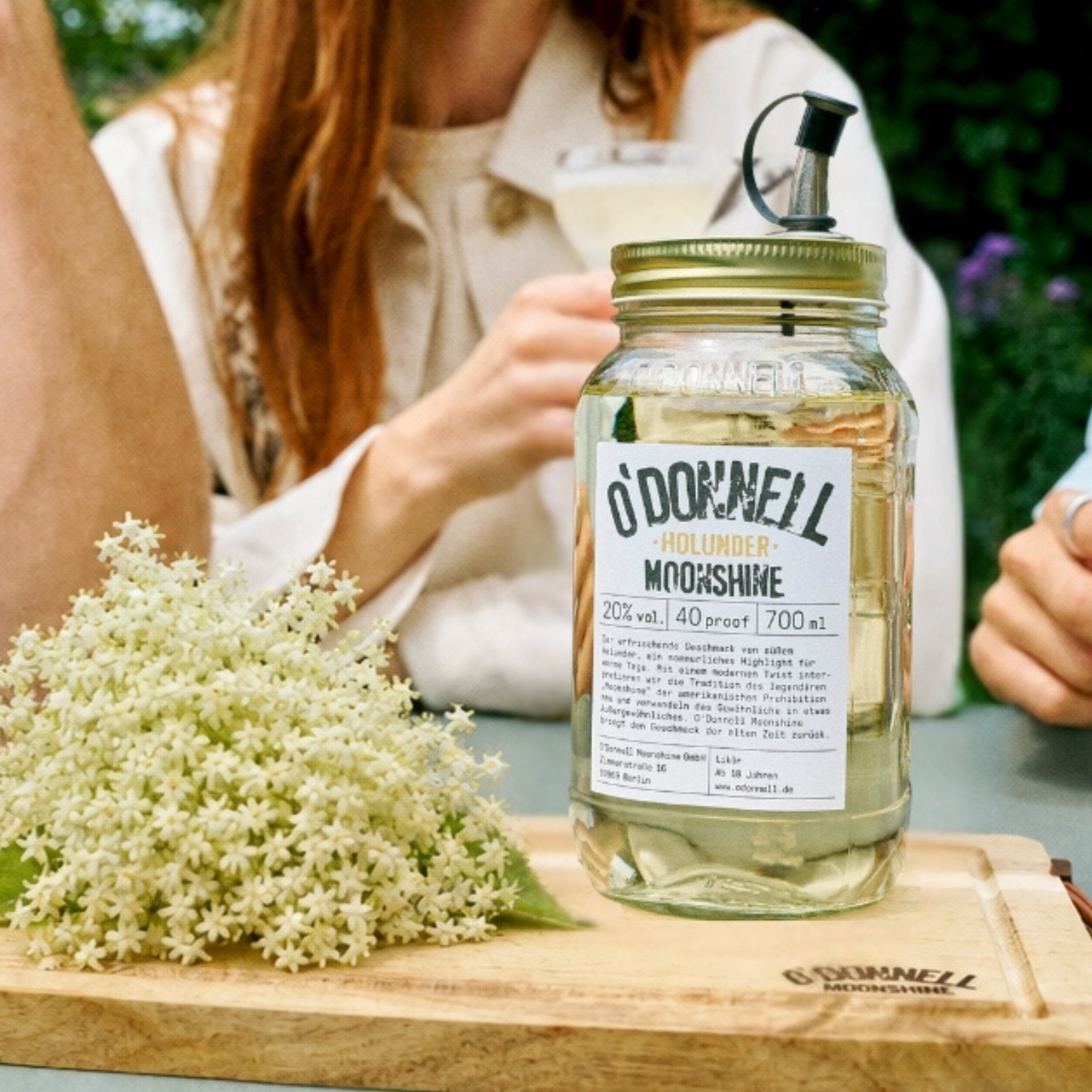 Der O'Donnell Moonshine Holunder im 700ml Mason Jar präsentiert neben einer reifen Holunbderblüte.